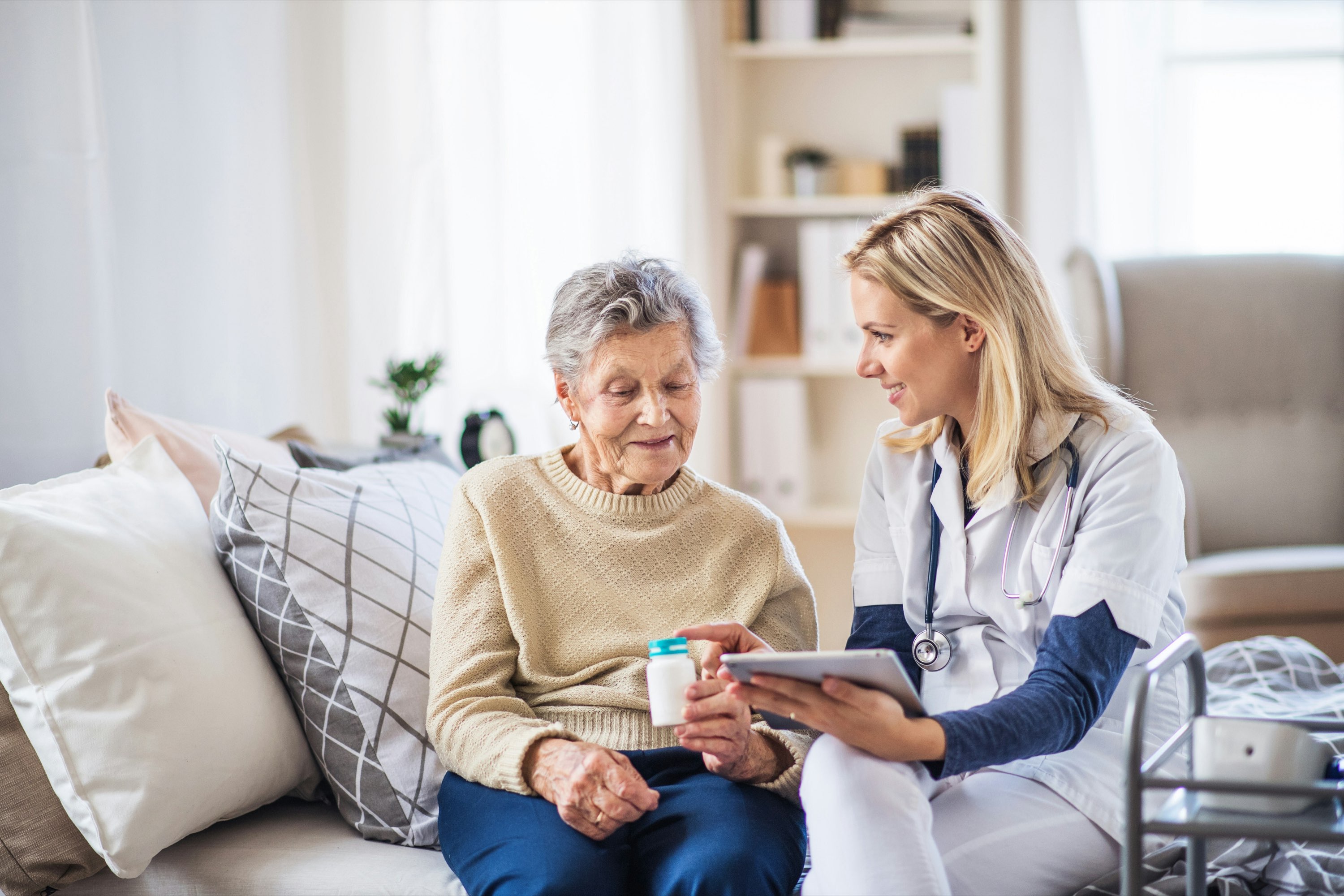 A home health nurse going over a medication with an older woman on her sofa