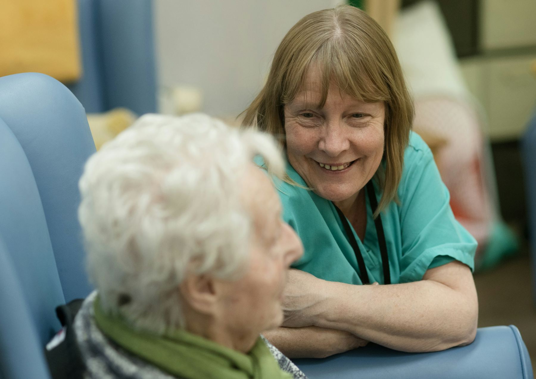 A carer in teal scrubs smiling with an older woman