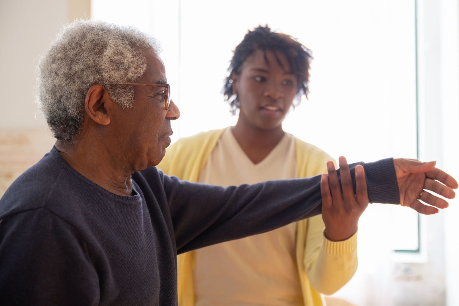 A caregiver helping an older man with arm exercises
